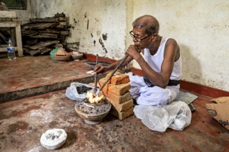 A man blows into a coal-fired pool with a concentrated face, a man burns sapphires in a small stove