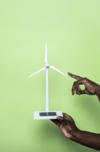 Close-up of a hand holding a small wind turbine model, symbolizing renewable energy innovation, set