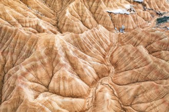 Aerial shot captures a striking desert landscape with rugged, eroded hills and vivid geological