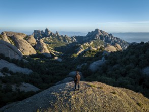 A person stands on a rocky hill, overlooking the stunning Montserrat mountains in Catalonia, Spain,