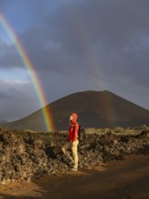 A woman in a red jacket stands on volcanic terrain in Timanfaya National Park, Lanzarote. A vivid