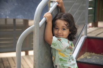 An happy toddler smiling and enjoying a playful day at the park. The child grips the playground