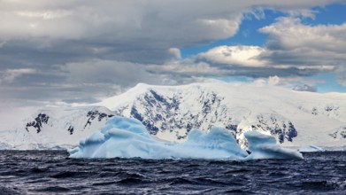 Icebergs floating in undulating water against a backdrop of snow-capped mountains under a dramatic