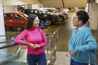 A young man and woman, both Gen Z, engage in a lively conversation in a parking area, displaying