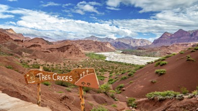 Red mountain landscape with vegetation and a sign in the foreground under a blue sky, The landscape