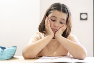 A young girl sits at a desk, appearing stressed and overwhelmed with her homework. Her head rests