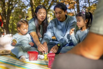 Asian family sharing a joyful picnic in a sunlit autumn park. They are seated on a blanket