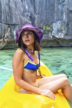 Young woman wearing a bikini and a purple hat enjoys kayaking in the crystal clear waters of twin