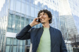 A businessman holds a phone to his ear while walking outside a modern glass building. The image