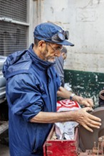 A man working on a machine in a workshop, wearing a blue jacket and a cap, A man sharpening knives