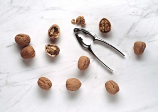 A scattered arrangement of whole and cracked walnuts with a metal nutcracker on a smooth marble