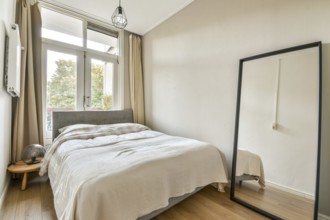 A stylish, serene bedroom featuring a bed with soft bedding, a large mirror, and bright natural