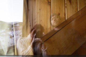 A woman with red hair holding a camera and a man are reflected in the glass window of a rustic