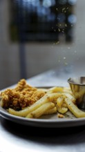 A close-up shot of crispy golden fries and crunchy chicken pieces on a plate. Fresh herbs are