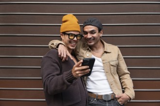 A Colombian gay couple smiles warmly as they look at a phone together. They are casually dressed,