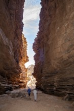 Two people walk through a narrow rocky gorge under a blue sky with clouds, rocky landscapes and