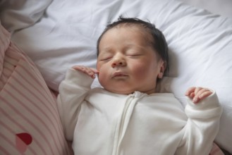 A serene newborn baby peacefully sleeps on a soft white pillow. The infant is dressed in a cozy