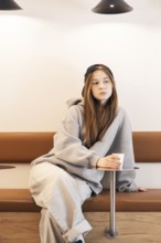 Teenage girl in casual attire with a cap, sitting thoughtfully on a bench. She holds a paper cup,