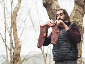 A man hangs clothes on a line in a forest, emphasizing simplicity and nature. The scene highlights