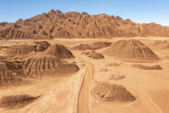 Aerial view of a vast desert landscape featuring a rugged mountain range and a winding dusty road