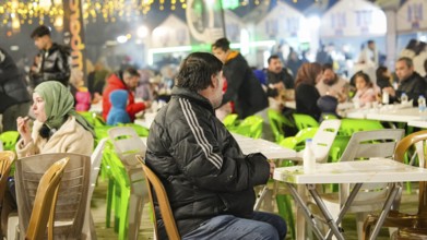 Muslim families and individuals gather at outdoor tables for a mass community Iftar meal under