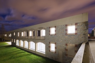 A beautifully illuminated stone hospital with arches under a twilight sky, showcasing architectural
