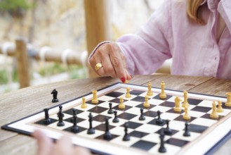 A close-up of hands moving chess pieces during a game played outside on a wooden table The board