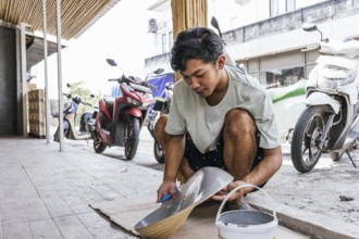 A Balinese artist skillfully paints a sculpture outdoors, blending traditional techniques with