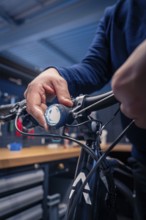Hand adjusts the light on the bicycle handlebars in a dark blue workshop, technical focus, Waldbike