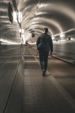 Man walking through an illuminated, tiled tunnel, old Elbe tunnel, Hamburg, Germany