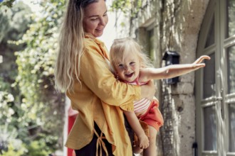 A joyful mother lovingly holds her daughter in an outdoor setting, surrounded by nature. The scene