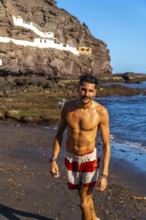 Young hispanic man walking on the beach of tufia, a coastal village of gran canaria, canary