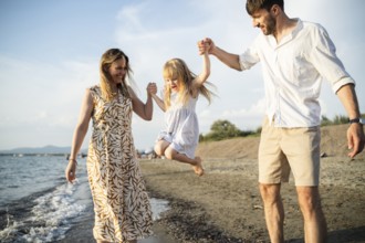 A cheerful family enjoys their time by the sea in Italy, as the parents swing their daughter into