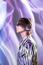 A young, trendy woman with short hair wears headphones while enjoying vibrant purple lighting. Her