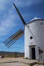 White windmill with a metal device of Don Quixote in front, under a clear sky, rural environment,