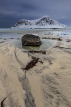 Rocks lying on the beach in front of snowy mountains, dark clouds, winter, Flakstadoya, Lofoten,