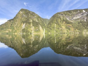 Mountains with reflections in the water against a blue sky in Doubtful Sound, South Island, New