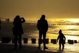 Winter on the North Sea, sunset at sea, beach walkers, coastal protection, through wooden posts,