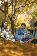 An Asian family enjoying a peaceful picnic surrounded by autumn foliage. They are sitting on a