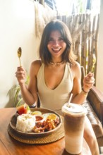Young woman holding cutlery and smiling, ready to enjoy traditional filipino breakfast with iced