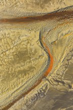 Aerial shot showing a textured, sandy desert terrain with orange streaks creating a river like