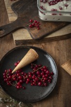 Top view of a rustic food scene featuring red currants on a dark plate beside a waffle cone, set