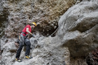 A climber scales a rugged rock face using traditional techniques, surrounded by impressive natural