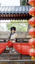 A woman in traditional Qing Dynasty attire stands gracefully on a decorated balcony in Pingyao,