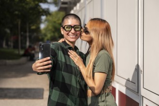 A joyful Colombian lesbian couple takes a selfie outdoors, showcasing their love and happiness.