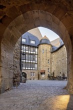 Through a stone Tor tor you can see a courtyard with a half-timbered house in the warm light of the