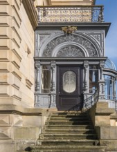 Historic door with filigree decorations and railings on a stone staircase in sunlight, Landau,