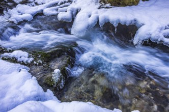 Small watercourse in winter with ice floes and mossy stones, Brühlbach below Urach Waterfall, Bad