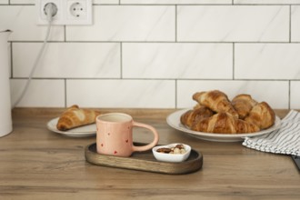 Freshly baked homemade croissants served on a wooden table with a cozy pink mug and a small bowl of