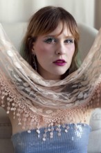 A woman with vibrant makeup and a sequined top poses gracefully, holding a delicate lace shawl Her